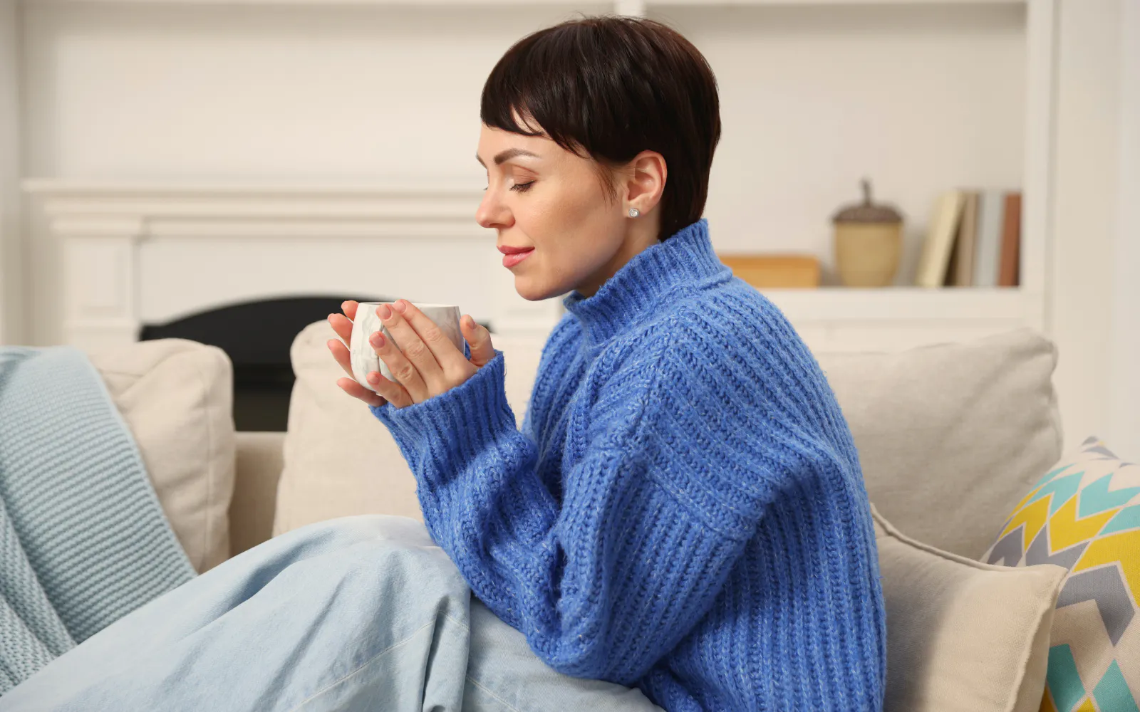 A woman sitting on a sofa with a hot drink, representing a happy homeowner after fogging treatments